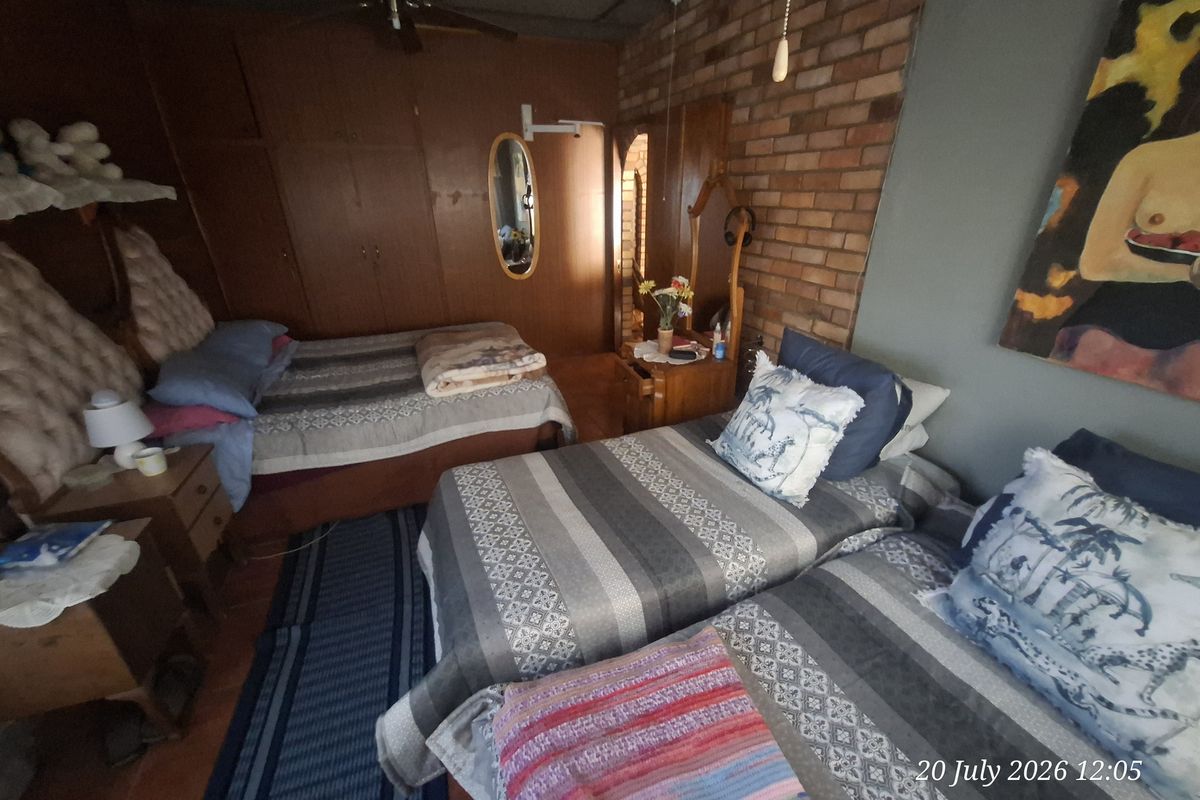 A bedroom featuring built-in wooden cupboards, an exposed brick feature wall, and a ceiling fan, offering a dated but functional living space.