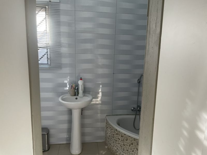 A functional bathroom featuring a pedestal basin, corner bathtub with decorative stone-look tiling, and wall-mounted shower fixtures.
