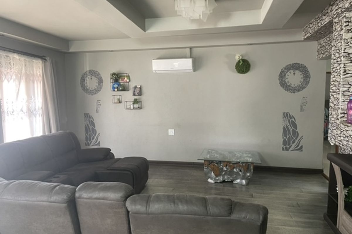 Spacious living room featuring a tray ceiling with recessed lighting, a split-system air conditioner, and a decorative stone-clad feature wall.
