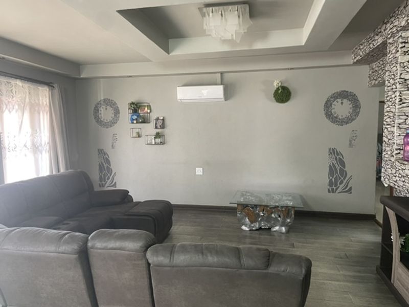 Spacious living room featuring a tray ceiling with recessed lighting, a split-system air conditioner, and a decorative stone-clad feature wall.