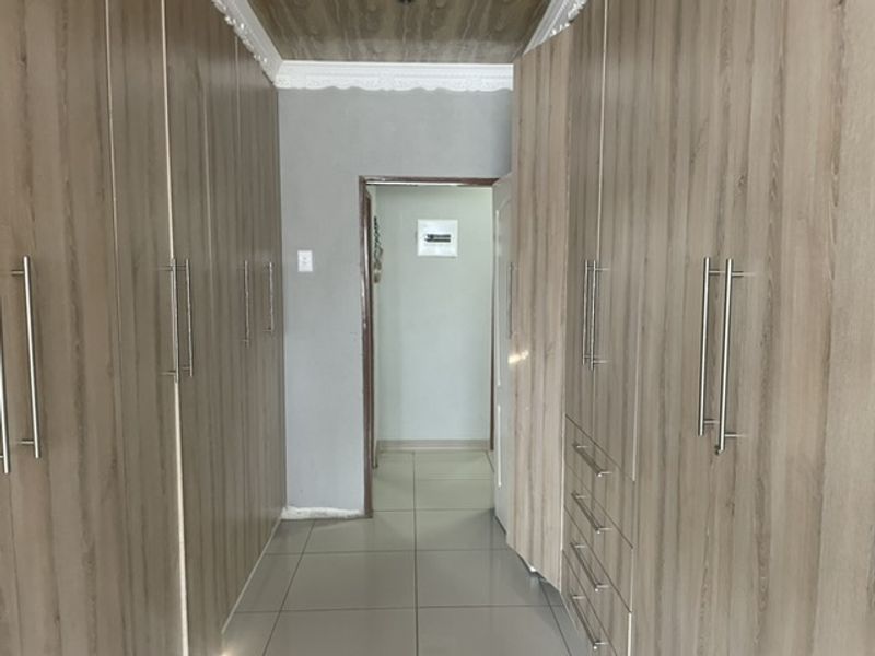 A hallway featuring extensive built-in wooden cabinetry, tiled flooring, and decorative ceiling cornicing, leading to an adjacent room with an electrical distribution board.