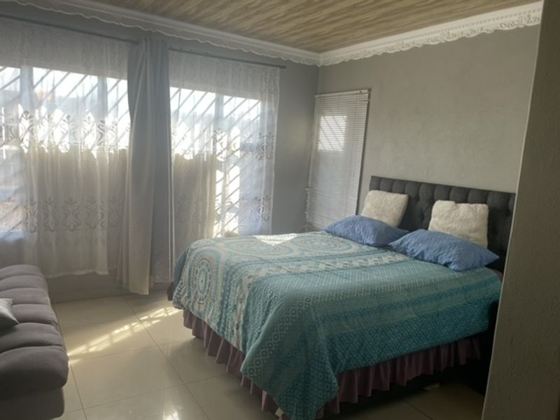 A bedroom featuring tiled flooring, decorative ceiling molding, and window security bars, providing a functional space with natural light.