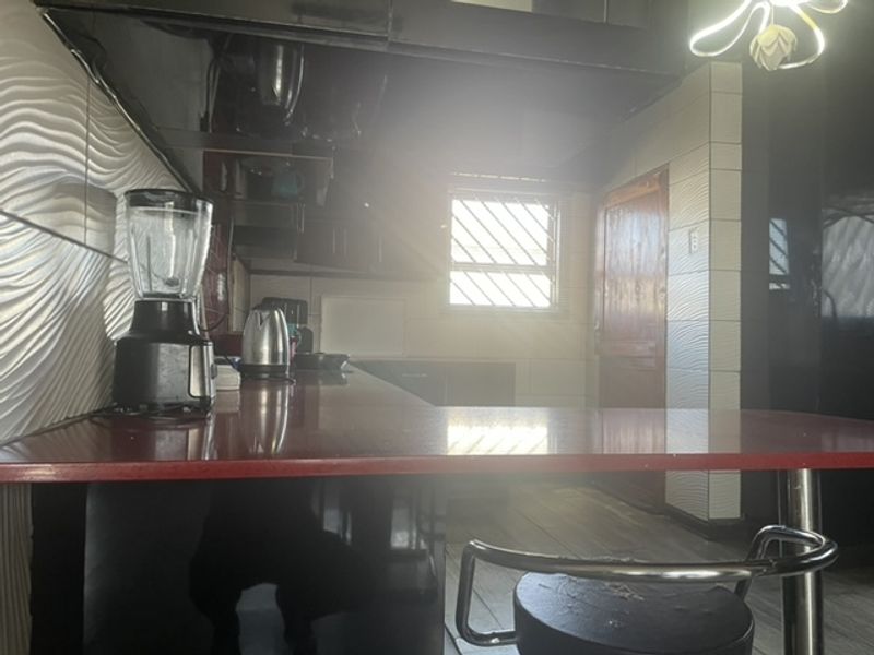 A kitchen area featuring textured wall tiles and a laminate countertop, currently suffering from poor lighting and dated finishes.