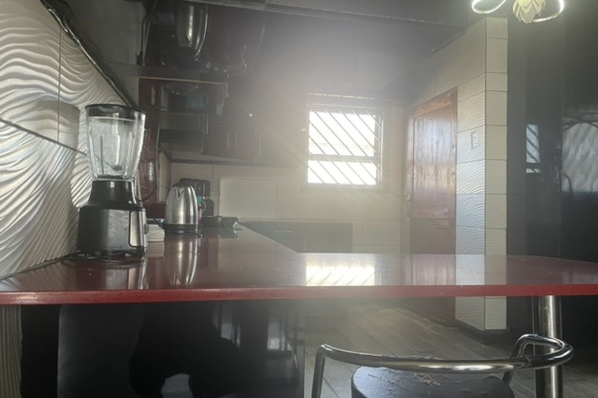 A kitchen area featuring textured wall tiles and a laminate countertop, currently suffering from poor lighting and dated finishes.
