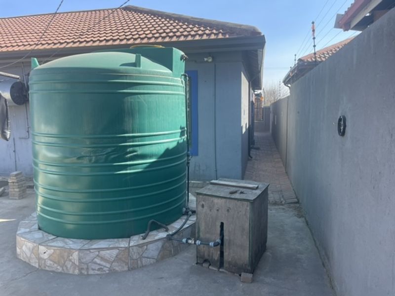Side exterior area featuring a large green water storage tank on a tiled base with an associated water pump system.