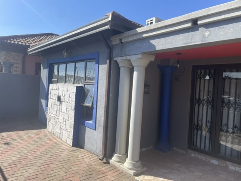 A rear exterior view featuring a paved patio area, classical columns, stone cladding accents, and secure metal gate access to the home.