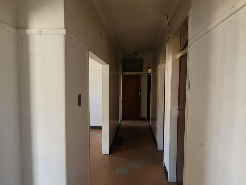 A vacant interior hallway featuring neutral walls, internal doors, and vinyl flooring, showing signs of wear and requiring cosmetic updates.