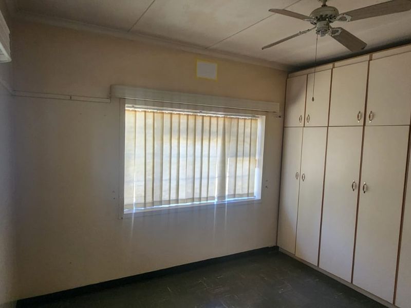 An empty bedroom featuring built-in cupboards, a ceiling fan, and an air conditioning unit, offering a blank canvas for renovation.