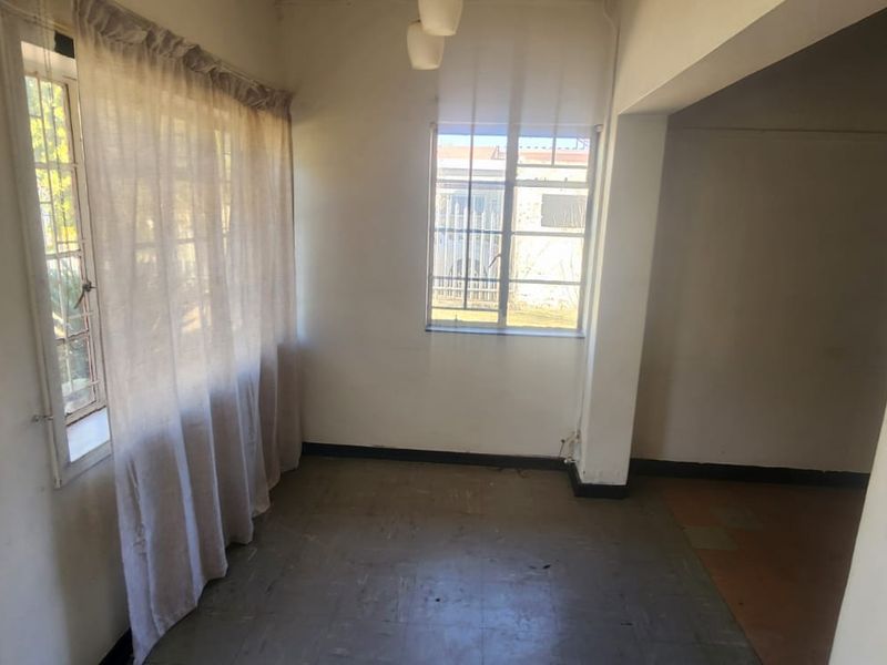 An empty, sunlit living area featuring steel-framed windows and tiled flooring, offering a blank canvas for renovation and interior design updates.