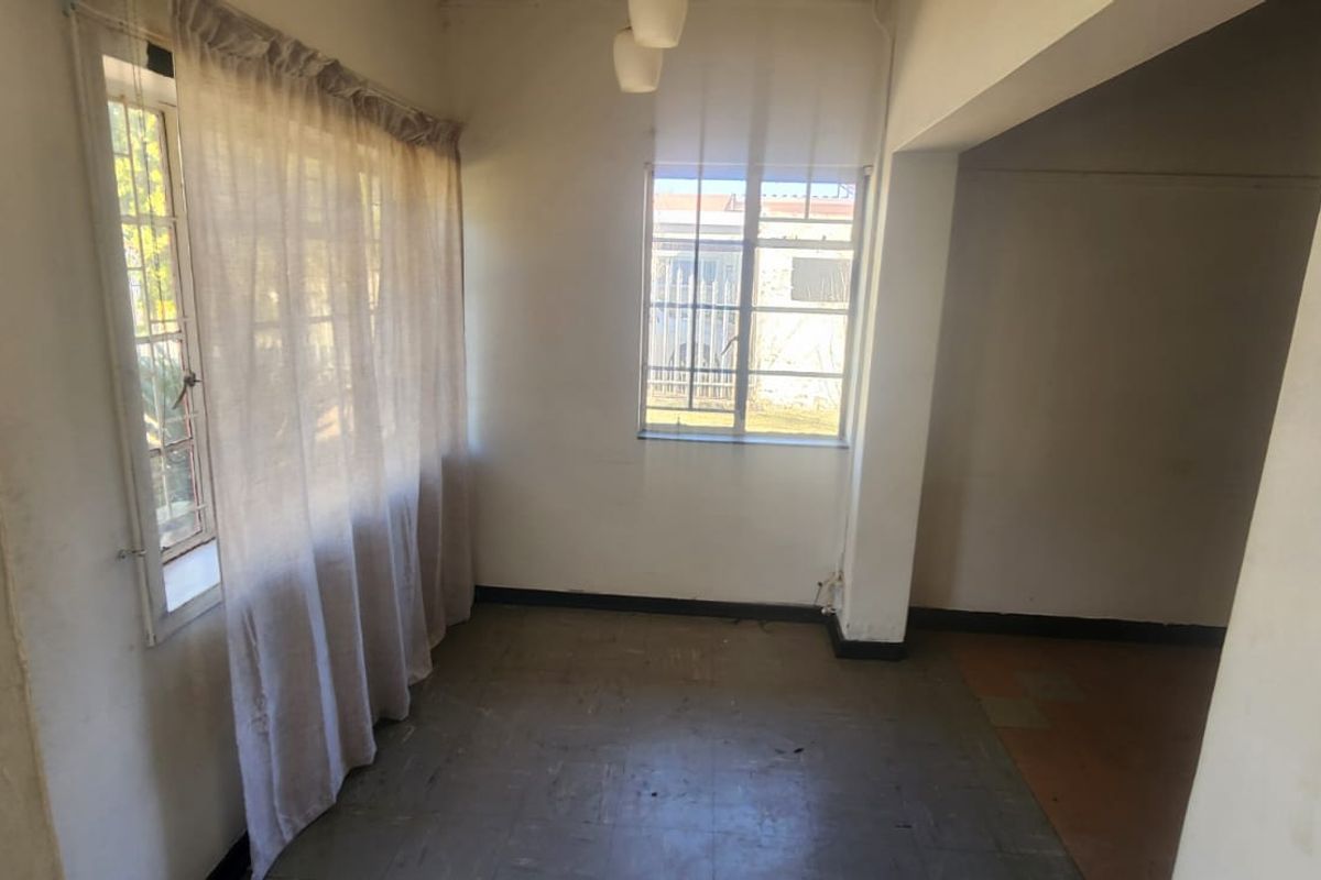 An empty, sunlit living area featuring steel-framed windows and tiled flooring, offering a blank canvas for renovation and interior design updates.