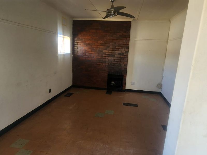 An empty living room featuring a brick accent wall, ceiling fan, and tiled flooring, requiring cosmetic updates to improve its overall condition.