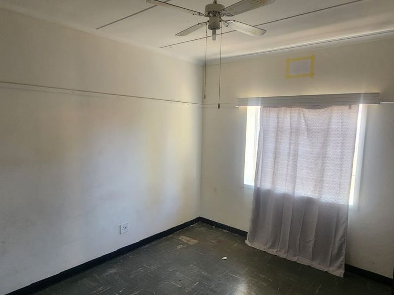 A vacant bedroom featuring a ceiling fan, picture rails, and worn vinyl flooring, requiring cosmetic updates and wall repairs.