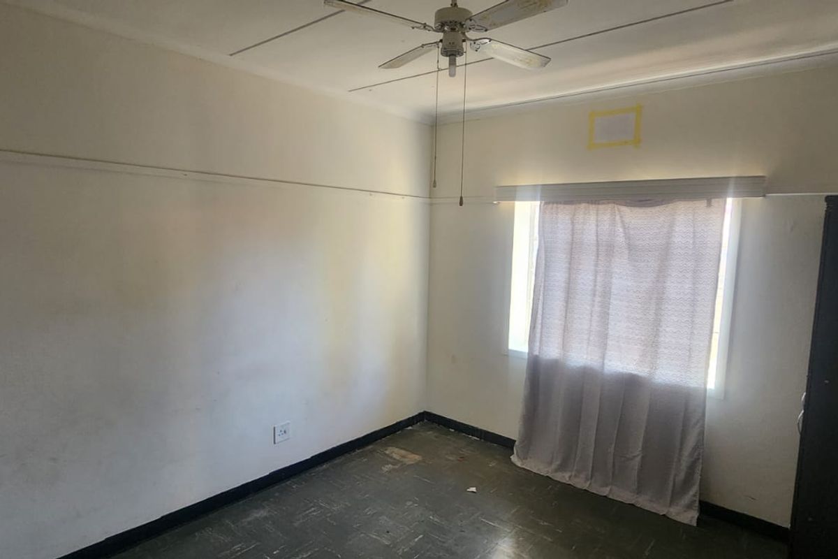 A vacant bedroom featuring a ceiling fan, picture rails, and worn vinyl flooring, requiring cosmetic updates and wall repairs.