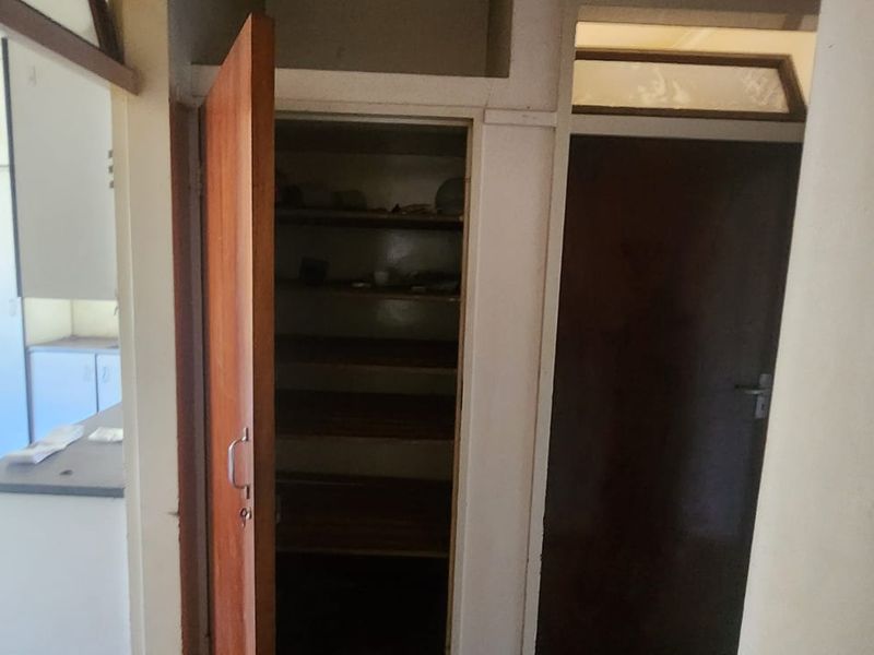 A functional scullery or pantry area featuring built-in shelving and internal access doors, providing additional storage space adjacent to the kitchen.