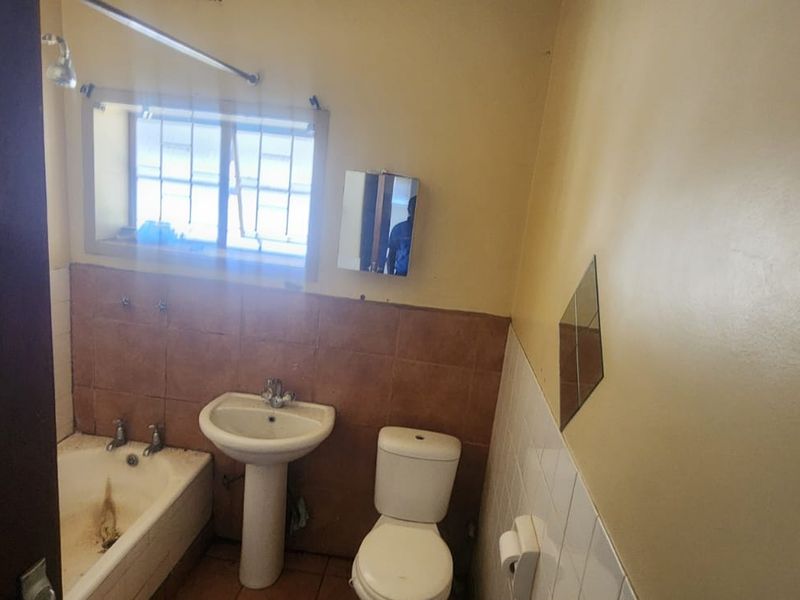 A functional bathroom featuring a pedestal basin, toilet, and bathtub with shower head, requiring cosmetic updates to modernize the space.
