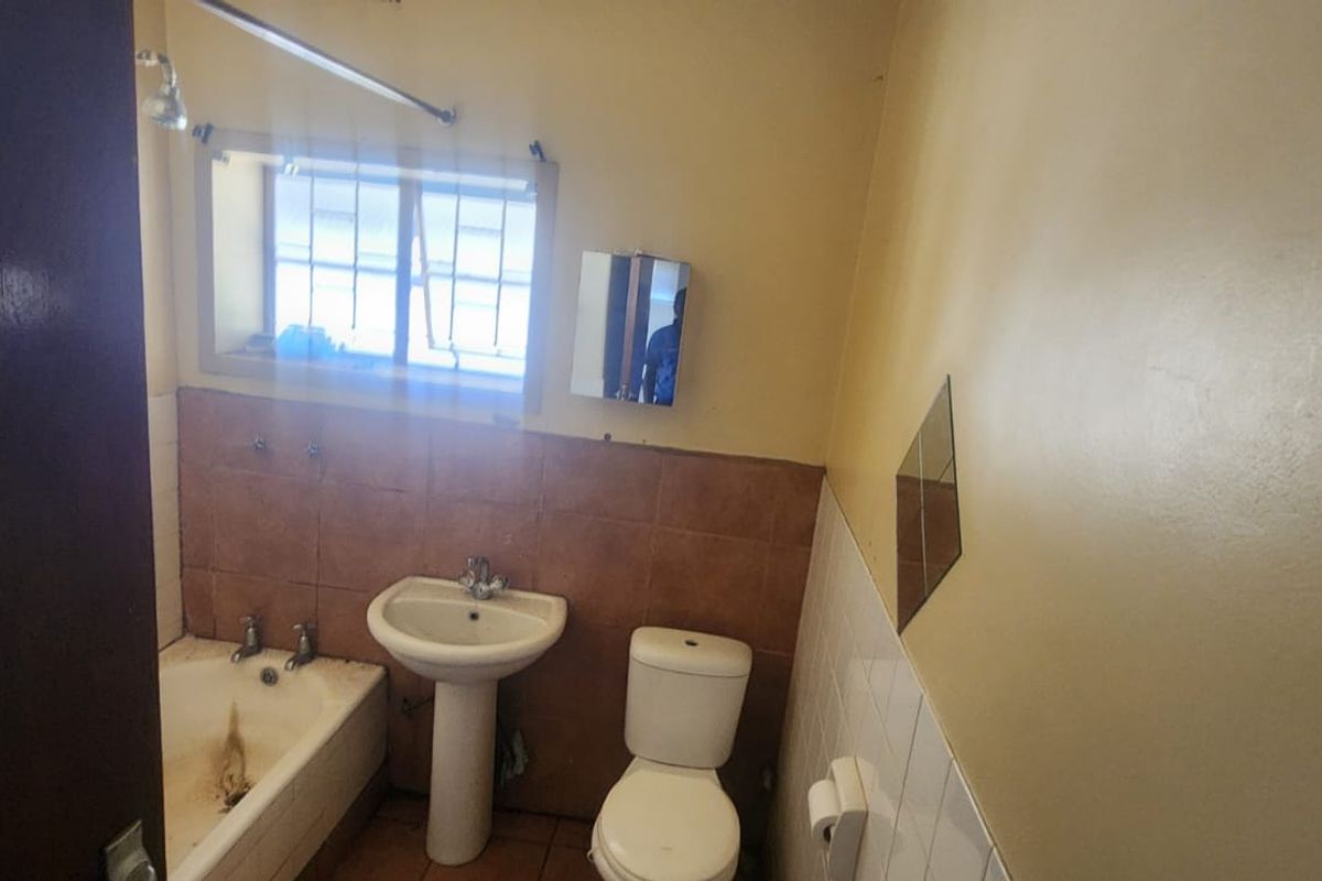 A functional bathroom featuring a pedestal basin, toilet, and bathtub with shower head, requiring cosmetic updates to modernize the space.