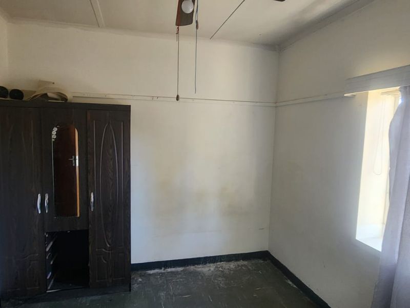 A bedroom featuring a ceiling fan and window with curtain rail, requiring cosmetic updates to the walls and flooring to improve its overall condition.