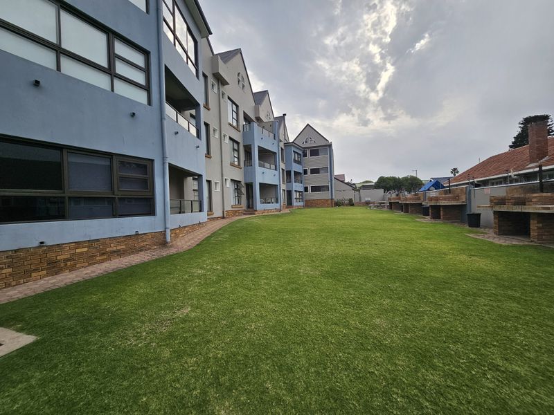 A well-maintained communal rear garden area featuring a large lawn, paved pathways, and multiple built-in brick braai stations for residents.