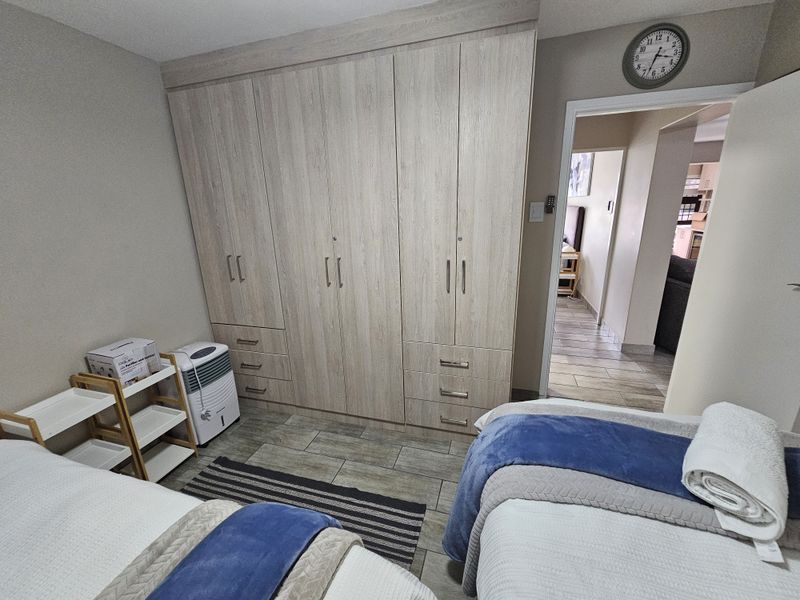 A well-maintained bedroom featuring light wood-finish built-in cupboards and durable tiled flooring, offering a clean and functional living space.