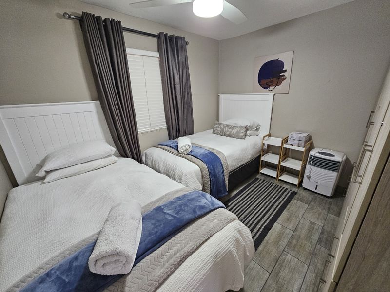 A well-maintained bedroom featuring tiled flooring, built-in cupboards, a ceiling fan, and window blinds, comfortably accommodating two single beds.