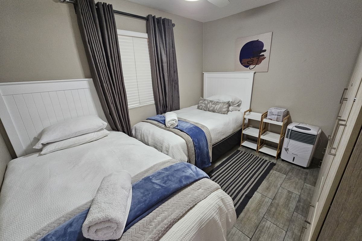 A well-maintained bedroom featuring tiled flooring, built-in cupboards, a ceiling fan, and window blinds, comfortably accommodating two single beds.
