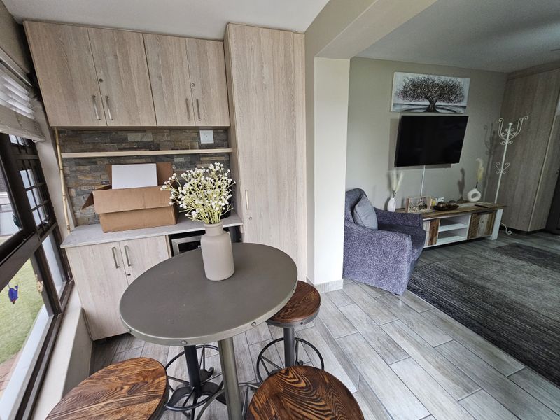 Open plan living area featuring light wood-look built-in cabinetry, stone tile backsplash, and modern tiled flooring, seamlessly connecting the kitchen and lounge space.