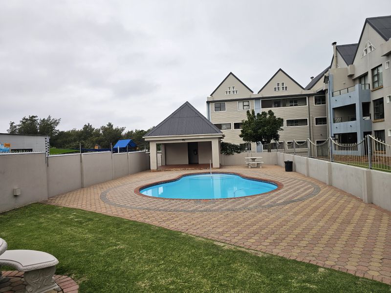 Communal pool area featuring a paved deck, a covered gazebo, and surrounding perimeter walls within an apartment complex.