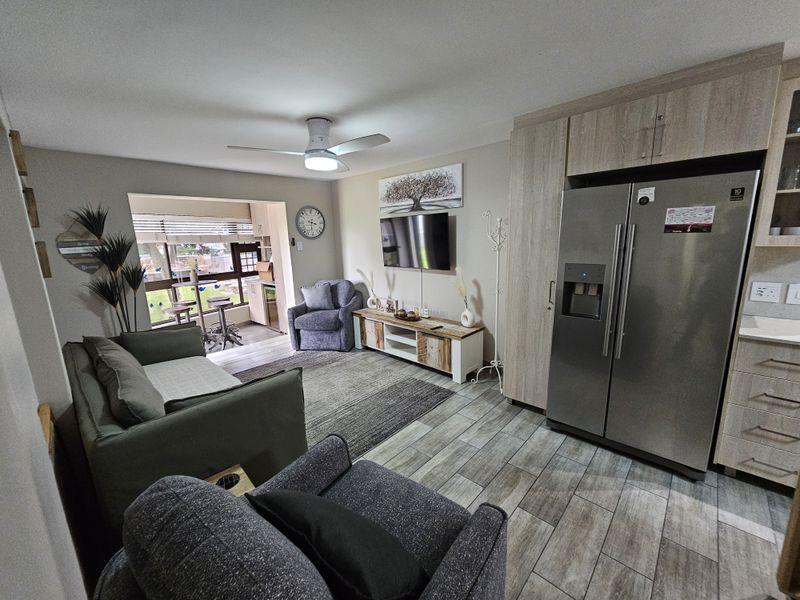 An open-plan living area featuring modern wood-look tiled flooring, built-in cabinetry, and a ceiling fan, seamlessly connecting to an adjacent sunroom space.