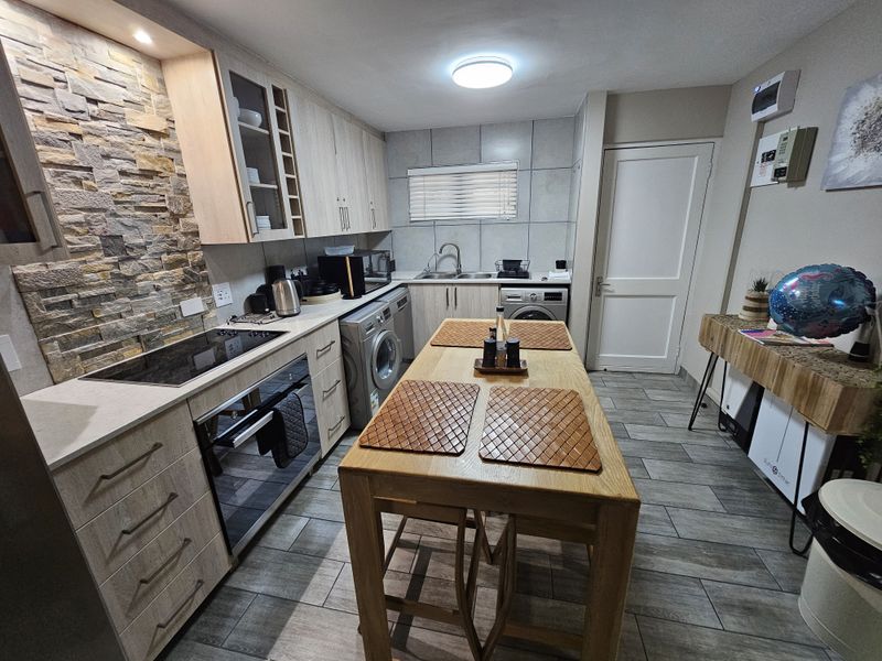 Modern kitchen featuring light wood cabinetry, stone veneer backsplash, integrated appliances, and convenient built-in laundry facilities with tiled flooring throughout.