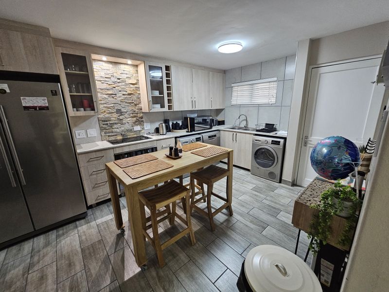 Modern kitchen featuring light wood cabinetry, stone veneer splashback, tiled flooring, and integrated appliances, offering a functional and contemporary cooking space.