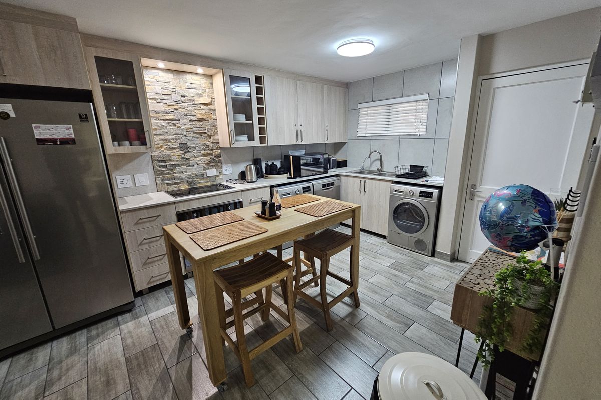 Modern kitchen featuring light wood cabinetry, stone veneer splashback, tiled flooring, and integrated appliances, offering a functional and contemporary cooking space.