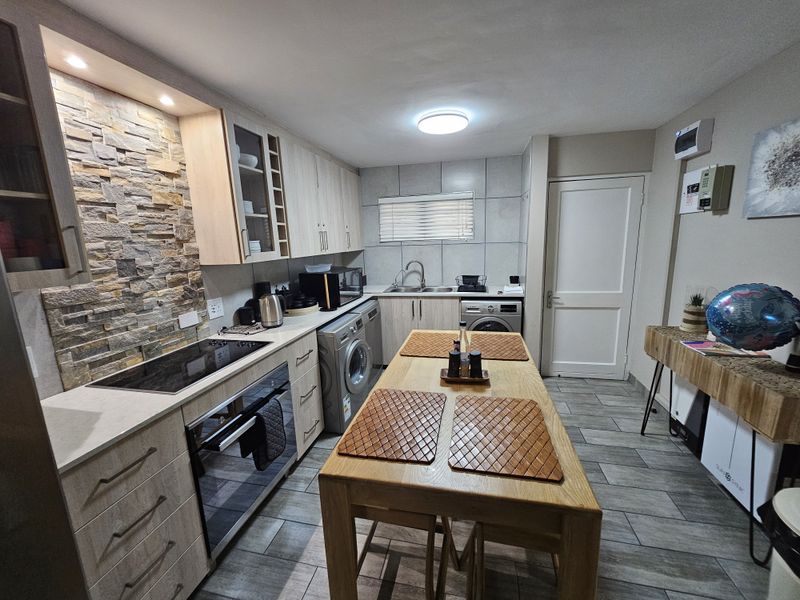 Modern kitchen featuring light wood cabinetry, stone veneer backsplash, integrated appliances, and tiled flooring with a functional layout.