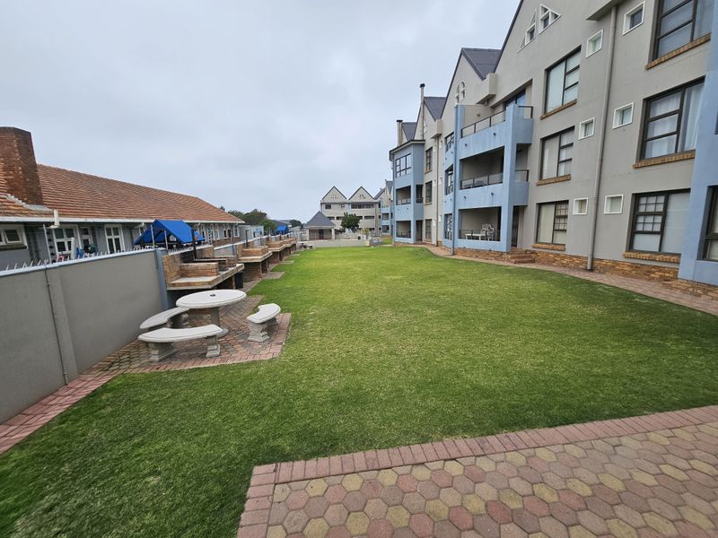 A well-maintained communal garden area featuring a paved patio with built-in brick braai facilities, set between apartment blocks.