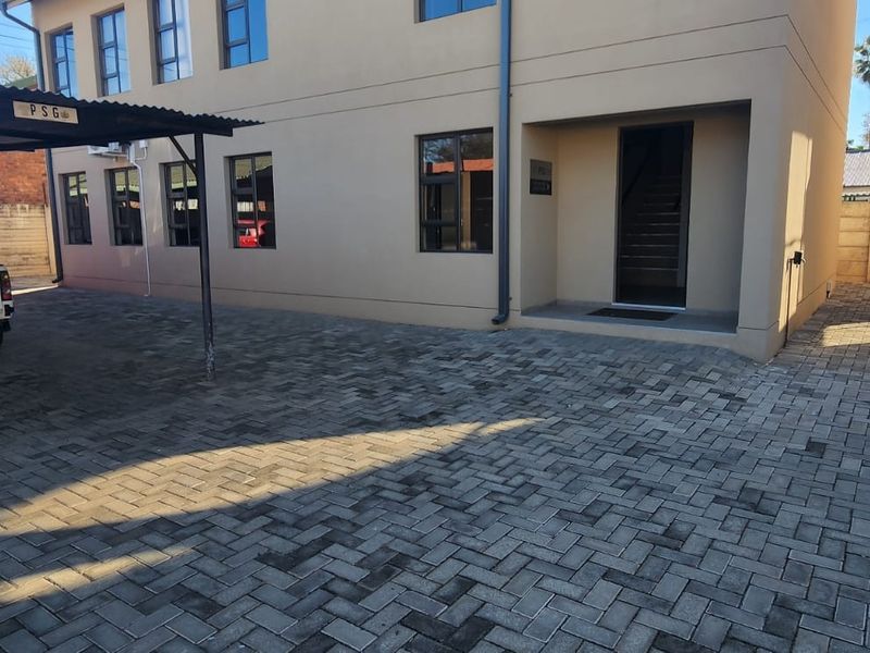 Exterior view of a commercial building featuring a paved driveway, covered parking area, and modern aluminium window frames.