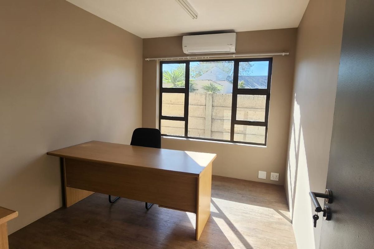 A functional office space featuring laminate flooring, a split-system air conditioner, and large windows providing natural light.