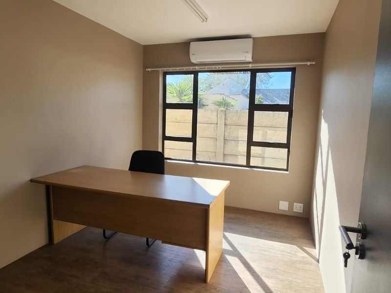 A functional office space featuring laminate flooring, a split-system air conditioner, and large windows providing natural light.