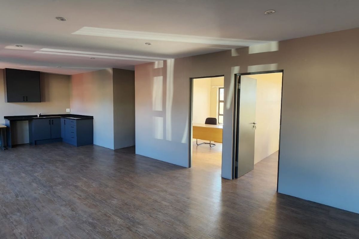 Spacious open-plan office area featuring a built-in kitchenette, modern laminate flooring, recessed lighting, and access to a separate private office space.