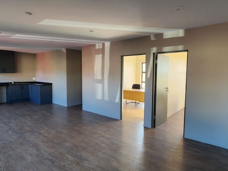 Spacious open-plan office area featuring a built-in kitchenette, modern laminate flooring, recessed lighting, and access to a separate private office space.