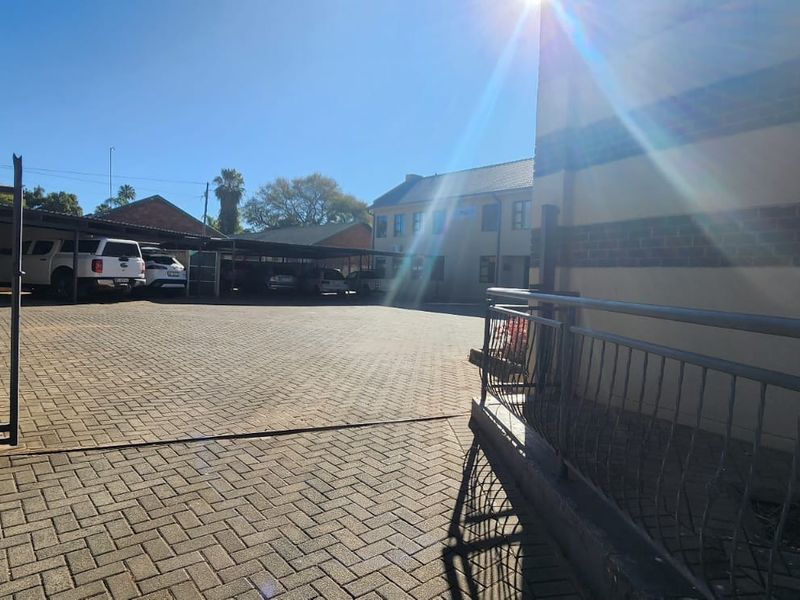 Exterior view of the property entrance featuring a paved driveway, covered carport parking area, and secure metal perimeter fencing.