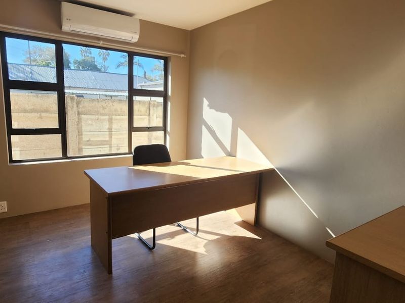 A functional office space featuring laminate flooring, aluminium-framed windows, and a wall-mounted air conditioning unit.