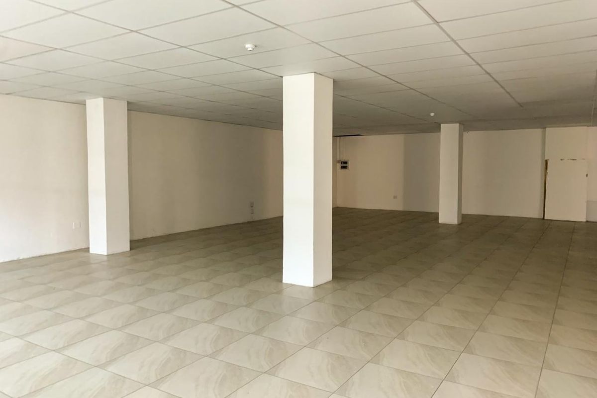 A spacious, vacant open-plan commercial area featuring neutral ceramic floor tiles, structural support columns, and a clean suspended ceiling grid.