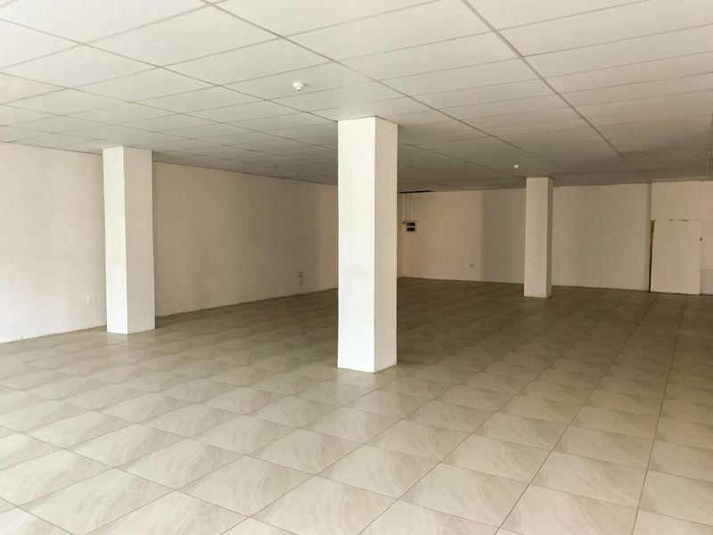 A spacious, vacant open-plan commercial area featuring neutral ceramic floor tiles, structural support columns, and a clean suspended ceiling grid.