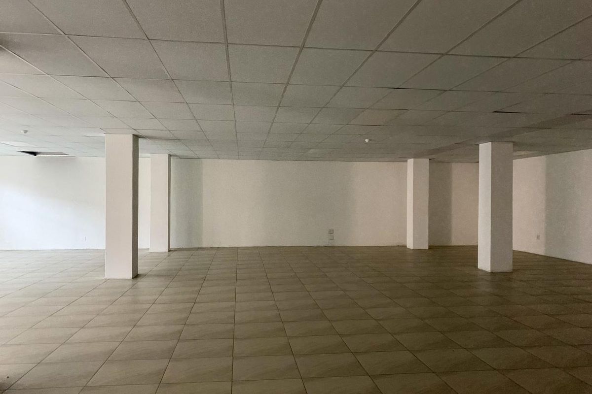 A large, vacant open-plan commercial space featuring ceramic tiled flooring, structural support columns, and a suspended ceiling grid.