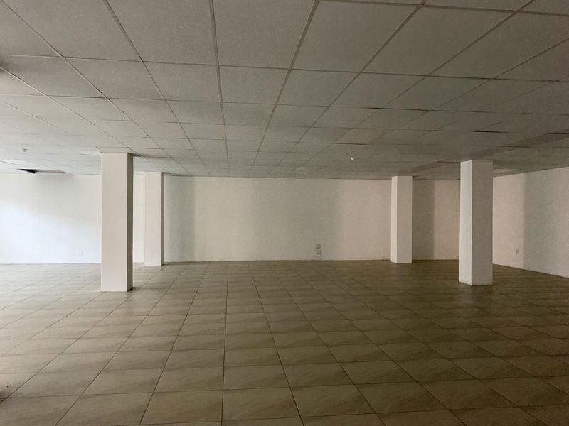 A large, vacant open-plan commercial space featuring ceramic tiled flooring, structural support columns, and a suspended ceiling grid.