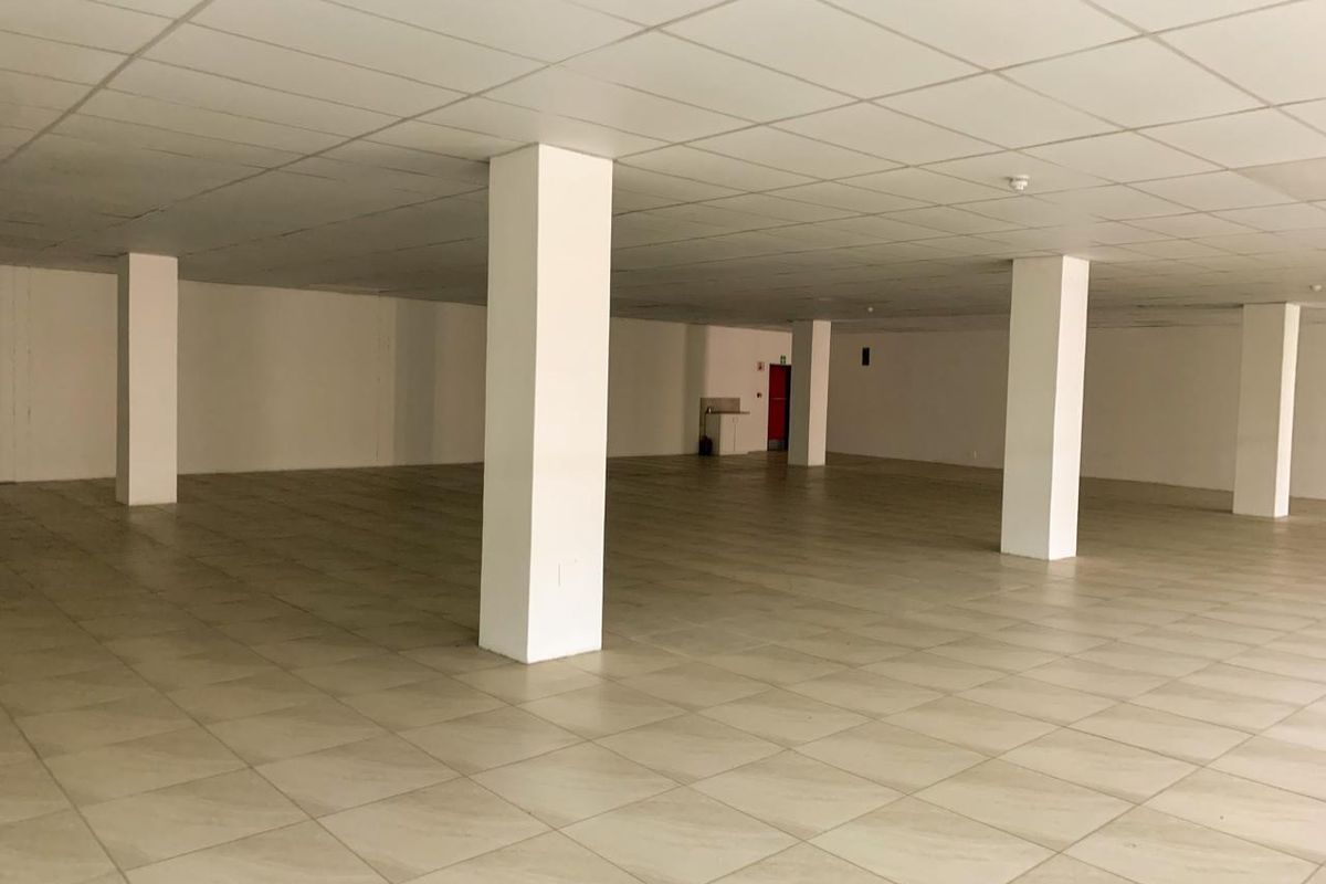 A spacious, open-plan commercial interior featuring neutral ceramic floor tiles, a suspended ceiling, and structural support columns, suitable for various business configurations.