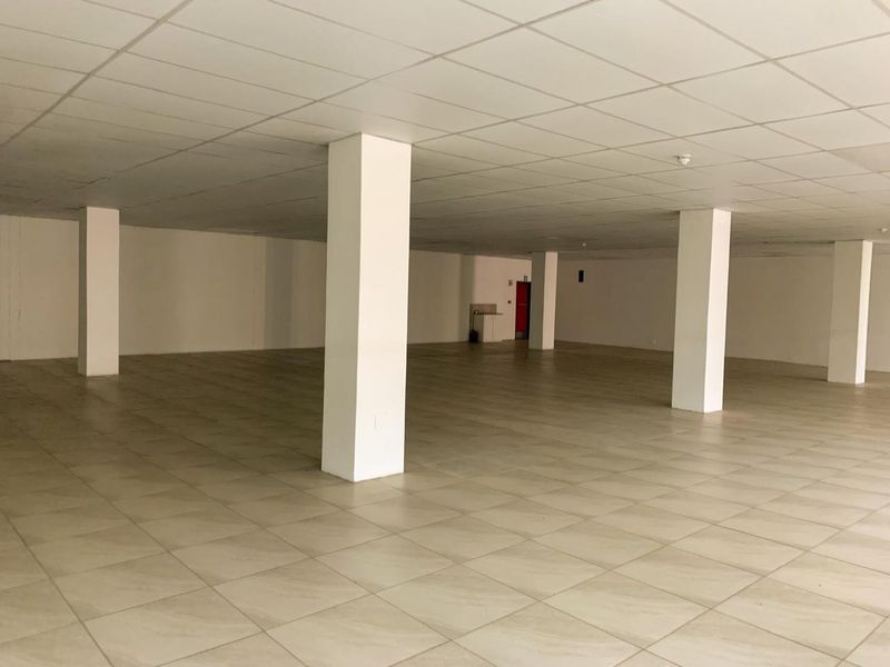 A spacious, open-plan commercial interior featuring neutral ceramic floor tiles, a suspended ceiling, and structural support columns, suitable for various business configurations.