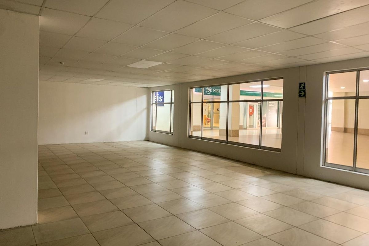 An empty commercial office space featuring large glass windows, ceramic tiled flooring, and a suspended ceiling, suitable for various business configurations.