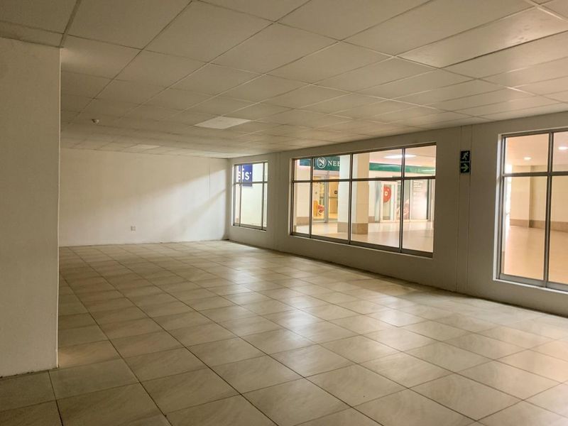 An empty commercial office space featuring large glass windows, ceramic tiled flooring, and a suspended ceiling, suitable for various business configurations.