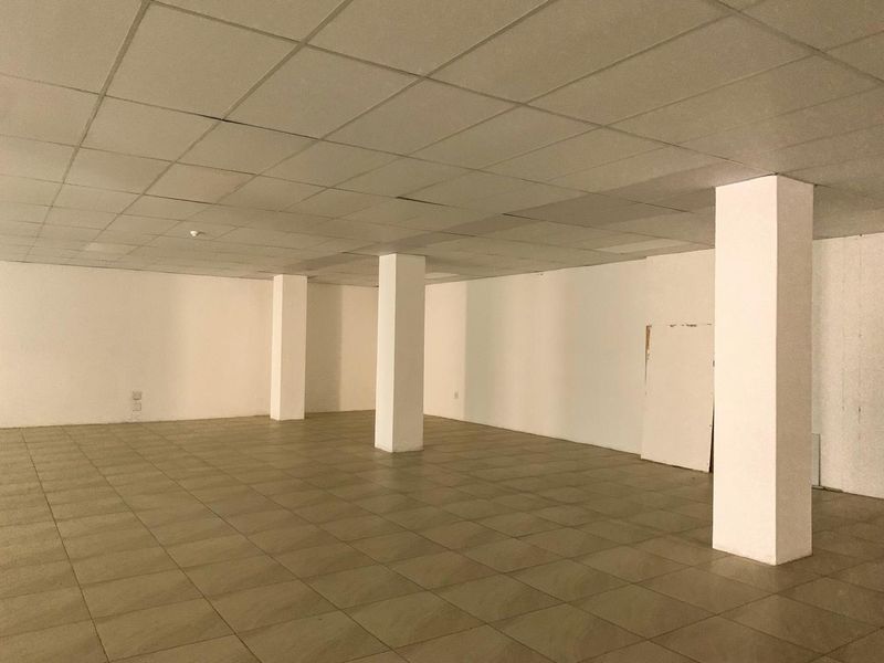 An empty, open-plan commercial space featuring ceramic tiled flooring, structural support columns, and a suspended ceiling grid.