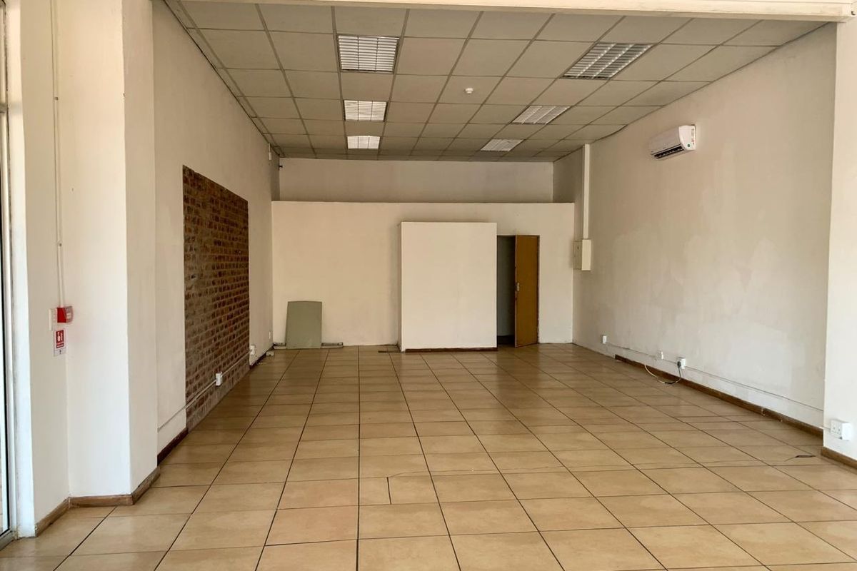 Open-plan commercial office space featuring ceramic tiled flooring, a suspended ceiling, and an exposed brick accent wall.